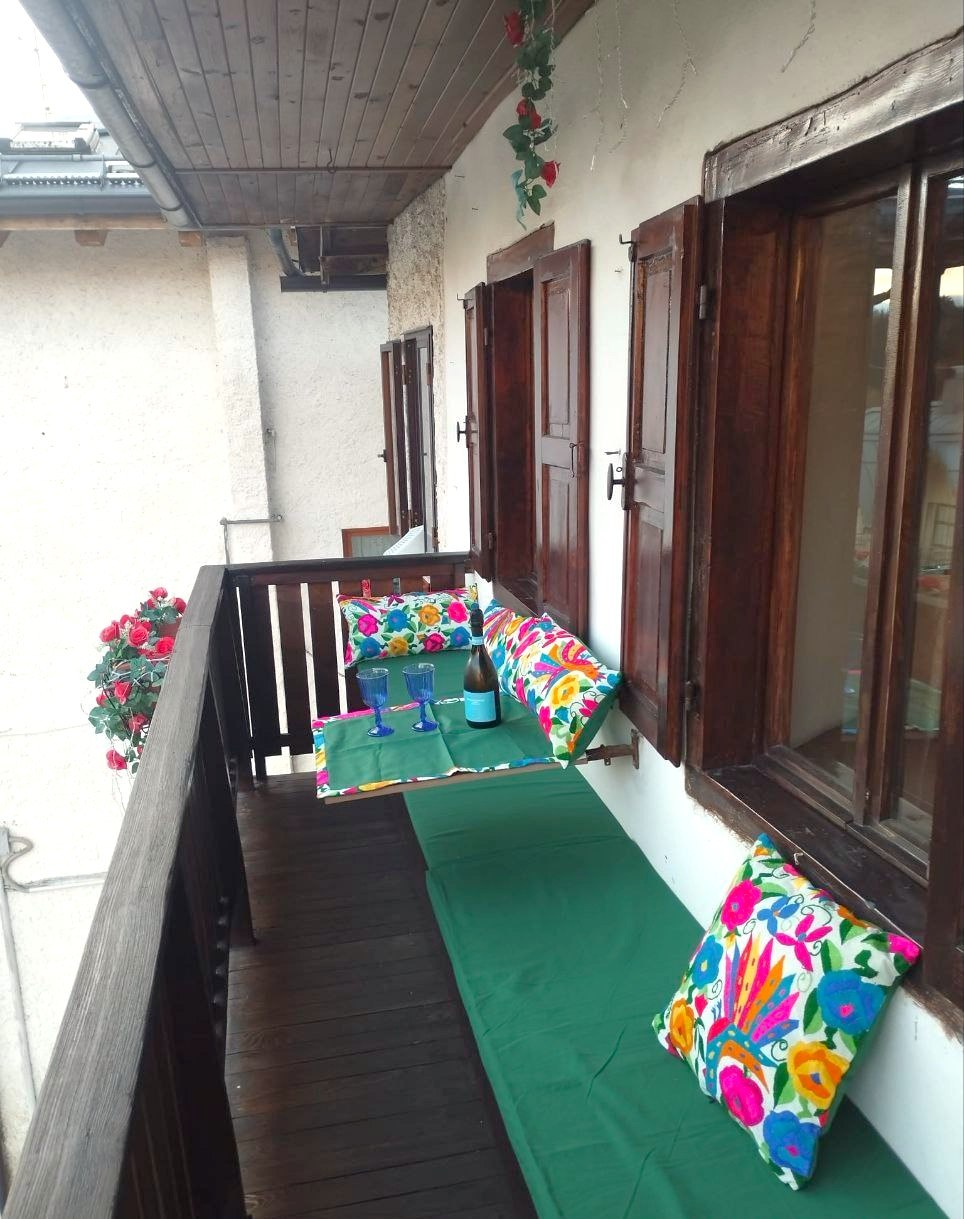Balcone di Rium Dolomiti allestito per aperitivo con cuscini colorati e bottiglia di vino